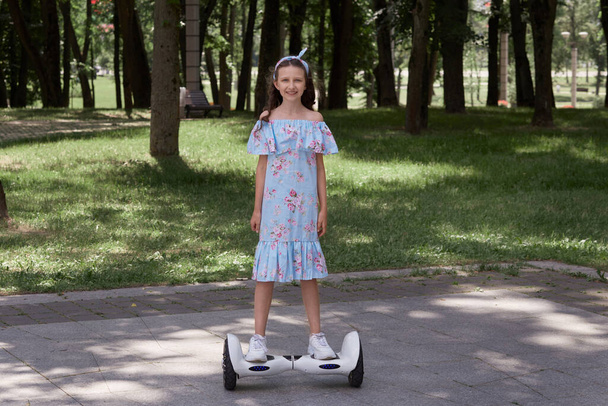 Teenage girl in a blue dress on a gyro scooter, hoverboard in a summer Park. - Fotó, kép