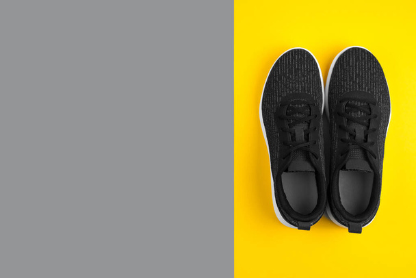Horní pohled na černé sportovní boty tenisky na žlutém a šedém pozadí. Sportovní koncept. Ploché. Prostor pro text. Trendy colors 2021 rok. - Fotografie, Obrázek