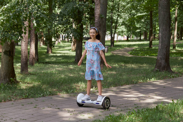 Een meisje in een blauwe jurk rijdt door het park op een gyroscooter. Lang haar. - Foto, afbeelding