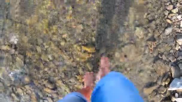Chica caminando descalza sobre piedras de río poco profundo primer plano, día de verano soleado - Imágenes, Vídeo