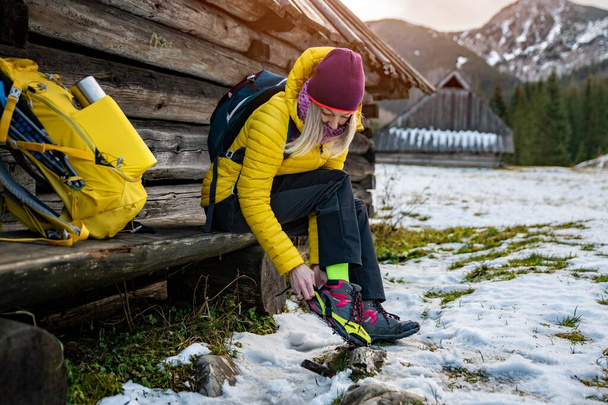 Білявка жінка альпіністка в жовтій куртці кладе судоми на своє взуття, перш ніж досягти вершини
. - Фото, зображення