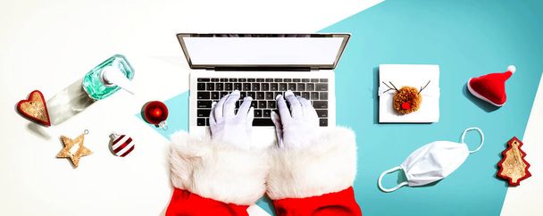Santa Claus using a laptop computer with a mask and a sanitizer bottle - Фото, изображение