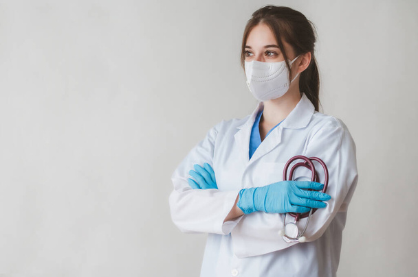 Portret młodej, pewnej siebie lekarki noszącej medyczną maskę do twarzy trzymającej stetoskop na białym tle - Zdjęcie, obraz