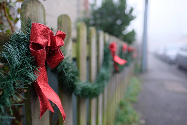 Festlich geschmückter Holzzaun mit roten Bändern, wenn die Dezember- und Weihnachtszeit naht - Foto, Bild