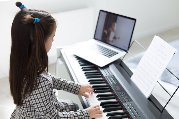 隔離中にピアノをオンラインで学ぶ少女の距離。コロナウイルスの概念. - 写真・画像