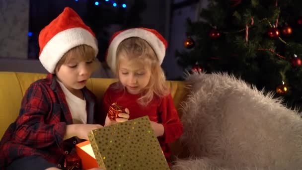 naughty little brother and sister in Christmas hats smile and hug - Filmati, video