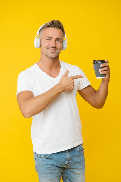 Fill your cup with flavor. Happy man point at coffee yellow background. Takeaway and cafe. Pointing finger gesture. Promoting and marketing. Morning drink. Modern technology. Dark and intense - Photo, Image