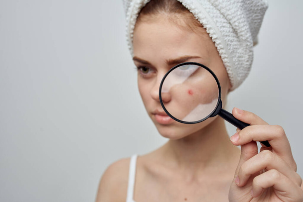 woman with a towel on her head magnifies pimple skin problems through a magnifier - Fotó, kép