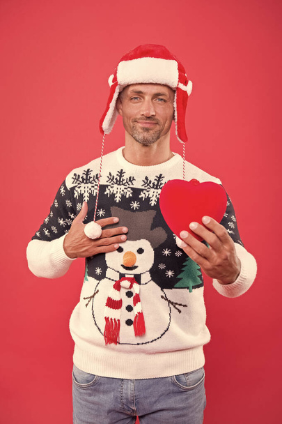 gift with love. sexy man santa earflap hat. man funny sweater red wall. warm your heart in winter. male share his heart. man ready for xmas party holiday. christmas is here. my new year gift for you - Foto, Imagem