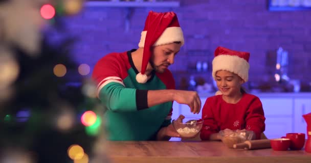 Boldog apa és kislánya mézeskalács tésztát gyúrnak karácsonyi sütikhez a konyhában. - Felvétel, videó