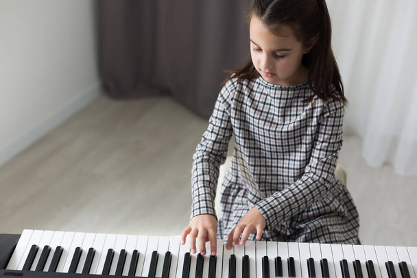 Cute little girl plays on piano, synthesizer. Training. Education. School. Aesthetic training. Elementary classroom. - Foto, Bild