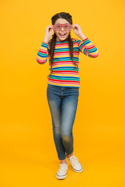 happy teen girl with braided hair wear casual style rainbow color and glamour party glasses on yellow background, optimist - 写真・画像