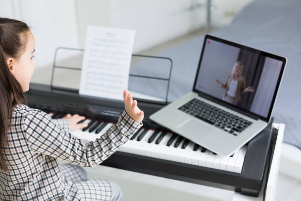 Маленька дівчинка дистанційно вчиться грати на піаніно під час карантину. Концепція Коронавірусу. - Фото, зображення