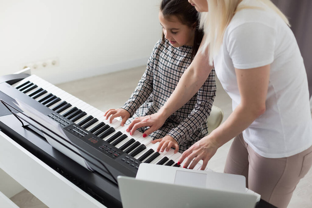 Mulher ajudando sua filha a tocar piano, corpo e botões do piano foram modificados digitalmente - Foto, Imagem