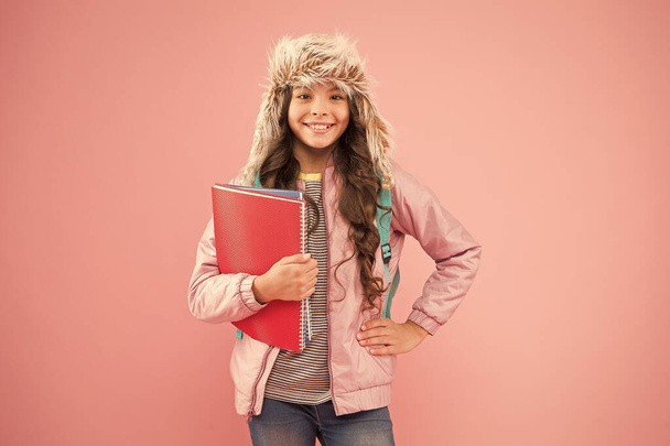 Work Hard. small happy girl earflap hat. back to school. winter holiday and vacation. kid warm clothes pink background. pupil daily life. schoolgirl carry backpack and books go home. no more exams - Valokuva, kuva