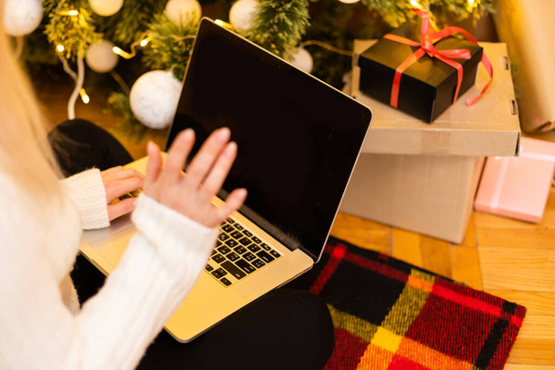 Frau mit Laptop auf dem Hintergrund eines Weihnachtsbaums nimmt Online-Glückwünsche für frohe Weihnachten entgegen - Foto, Bild