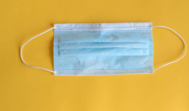 One disposable medical protective mask in blue with an ear loop to cover the mouth and nose to protect against bacteria on a yellow background - Foto, immagini
