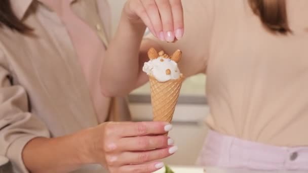 Midsection gros plan des mains féminines décorant cône de gaufrettes fraîches de crème glacée vanille avec des noix sur le dessus - Séquence, vidéo