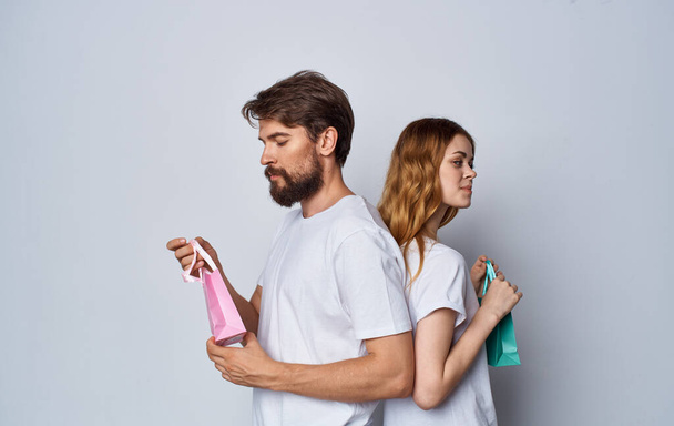 мужчина и женщина с подарочными пакетами стоят спиной друг к другу на сером фоне - Фото, изображение