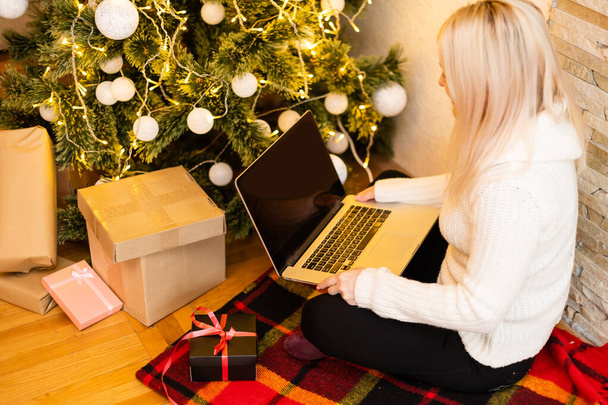 Foto di una bella donna bionda seduta su un divano con un computer portatile per fare acquisti per regali di Natale. - Foto, immagini
