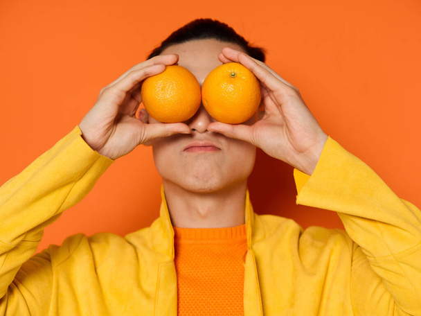 man met oranje sinaasappels in handen en emoties gele jas geïsoleerde achtergrond - Foto, afbeelding