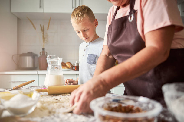 Жаждущий внук смотрит, как его бабушка месит тесто для печенья - Фото, изображение