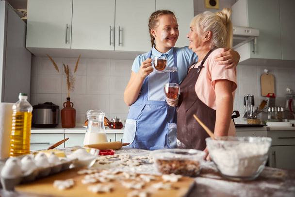 Přátelský dívka dává její babička velké objetí v kuchyni - Fotografie, Obrázek