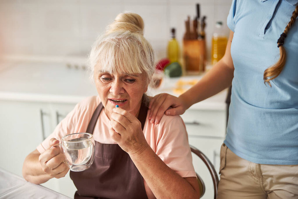 La abuela perturbada tomando su medicación con agua - Foto, Imagen