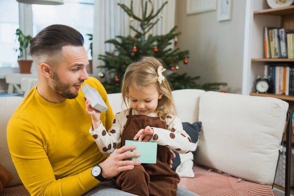 Młody ojciec daje pudełko prezentów małej córeczce malucha na Boże Narodzenie. - Zdjęcie, obraz