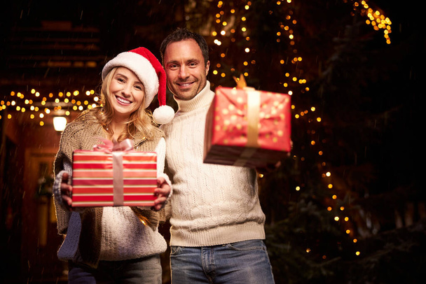 Beautiful lovely couple with red present boxes in hands enjoying great evening in Christmas - Foto, imagen