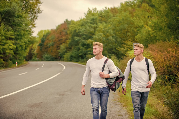 Man with backpack hitchhiking on road. Summer vacation. Tourist traveler travel auto stop. Budget travelers. men backpacks walking together by road. twins walking along road. Adventure and discovery - Foto, Imagem