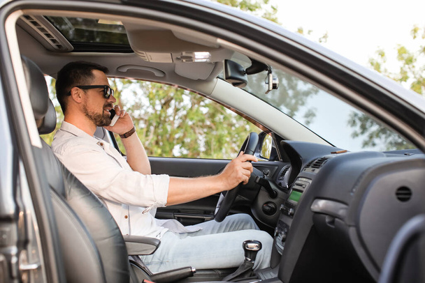 Jóképű férfi beszél mobiltelefonnal a modern autóban - Fotó, kép
