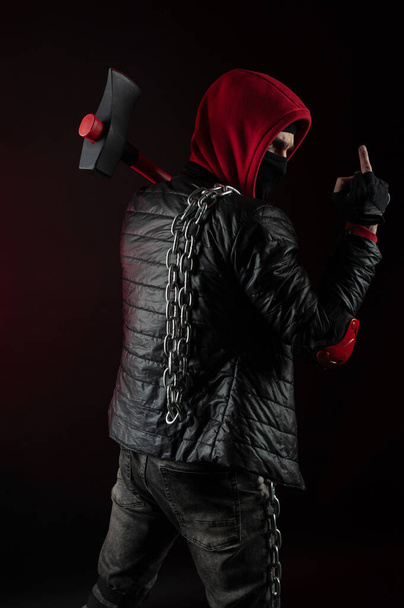 Egy férfi maszkban, fejszével a kapucnis kapucnis pulóverben, egy protestáns képe mutatja a középső ujjat. - Fotó, kép