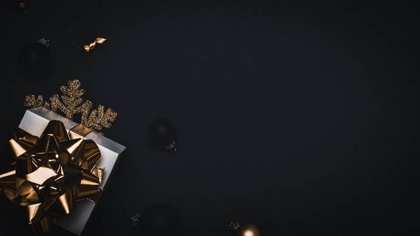 Decoración de Navidad. Regalo blanco con lazo dorado, bolas de oro y guirnalda de luces brillantes en decoración navideña sobre fondo oscuro para tarjeta de felicitación. Plano, vista superior, espacio para copiar - Foto, imagen