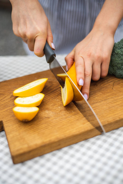 ナイフで若い季節のズッキーニを切った女性の手は、木製のまな板にスライスに.ズッキーニのスライス。野菜の調製方法。旬の食材、収穫。健康的な栄養、食事. - 写真・画像
