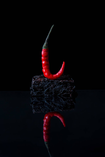Brownie díszített piros fűszeres chili paprika reflektív fekete felületen - Fotó, kép