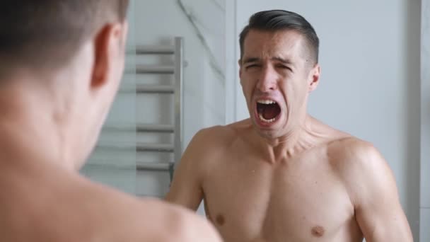 Trieste eenzame man kijkt wanhopig naar zichzelf in de badkamerspiegel. jonge hopeloze man schreeuwt met verdriet in hysterische en zenuwinzinking. - Video