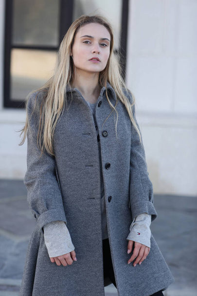  blond model girl with long hair in coat close up portrait on on city architecture background - Fotó, kép