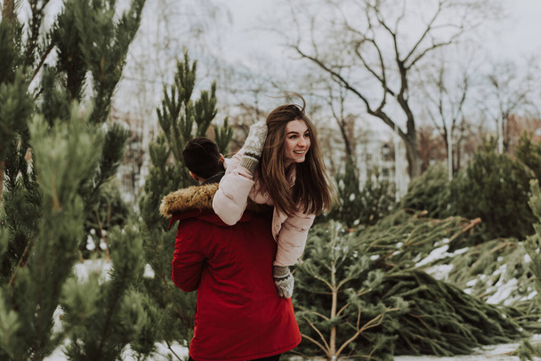 Hermosa joven caucásico heterosexual pareja de compradores están eligiendo y haciendo una compra en el mercado de árboles de Navidad en invierno al aire libre en clima nevado - Foto, imagen