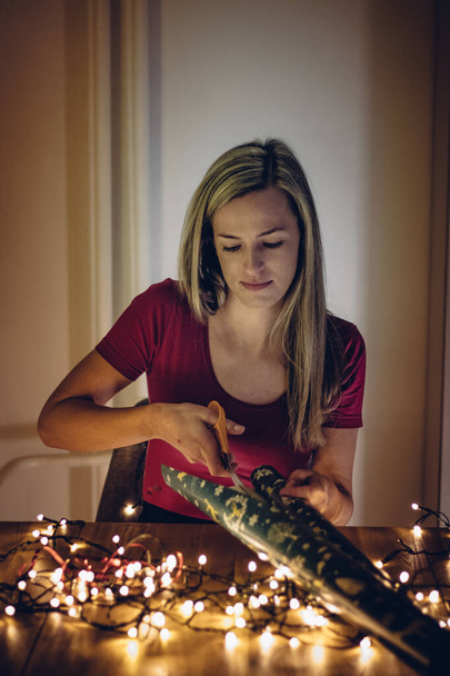 ハイライトの髪の女の子は、彼女が正確に包装紙をカットするかどうかを確認するために熱心に見えます。クリスマスと誕生日のプレゼントを包む。右のギフトを包むために魔法のペーパーを準備しなさい。メリー・クリスマス. - 写真・画像