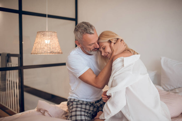 Grey-haired man hugging a blonde woman and looking romantic - Foto, Imagen