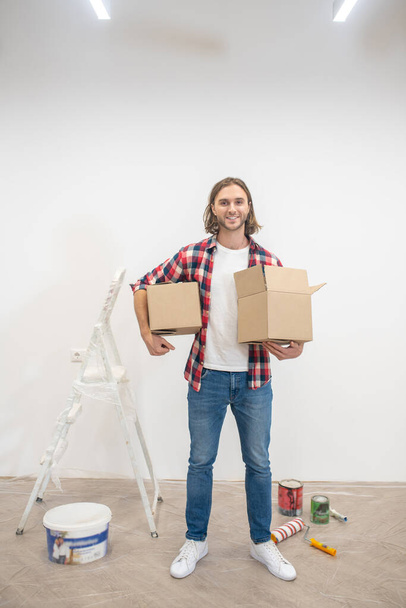 Long-haired man standing near the wall with boxes in hands - Valokuva, kuva