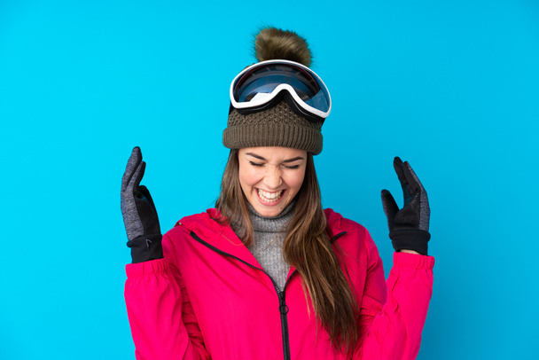 Дівчина-підліток лижниця зі сноубордистськими окулярами над ізольованим синім фоном сміється
 - Фото, зображення