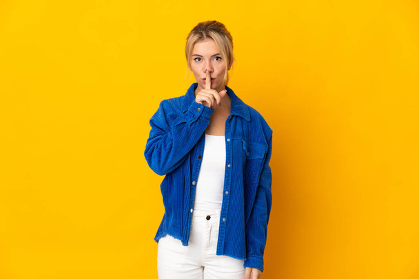 Young Russian woman isolated on yellow background showing a sign of silence gesture putting finger in mouth - Фото, изображение