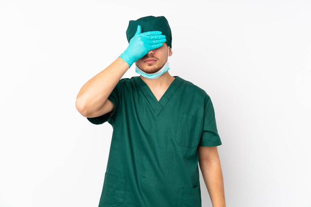 Chirurg in groen uniform geïsoleerd op geïsoleerde witte achtergrond die ogen met de handen bedekt. Ik wil niets zien. - Foto, afbeelding