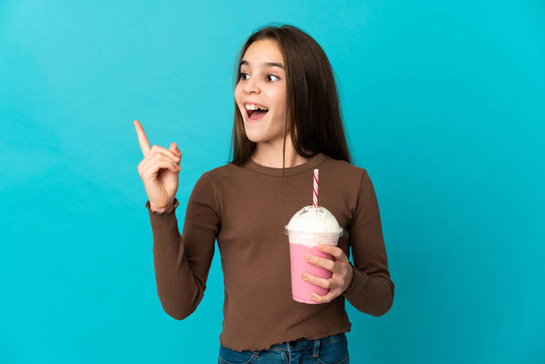 Маленькая девочка с клубничным молочным коктейлем изолирована на синем фоне, намереваясь реализовать решение, поднимая палец - Фото, изображение