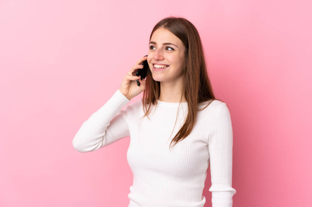 Mladá žena nad izolované růžové pozadí vedení konverzace s mobilním telefonem - Fotografie, Obrázek