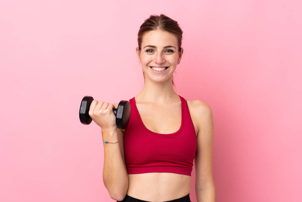 Giovane donna sportiva su sfondo rosa isolato rendendo sollevamento pesi - Foto, immagini
