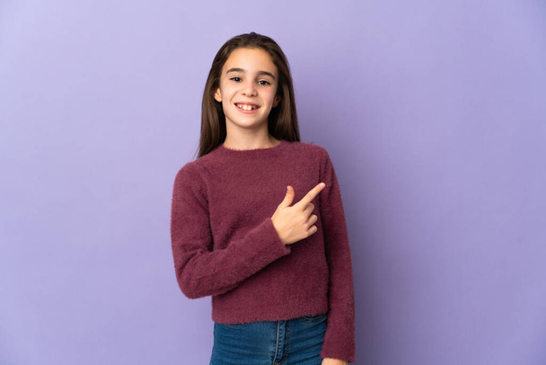 Little girl isolated on purple background surprised and pointing side - Foto, Imagem