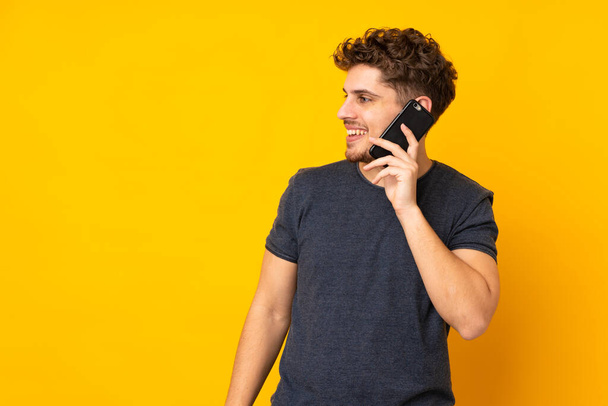 Молодой кавказский мужчина на изолированном фоне ведет разговор с кем-то по мобильному телефону - Фото, изображение
